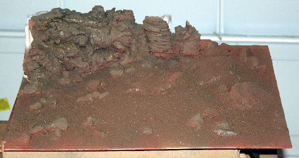 Having forgotten to take a picture of the intermediate stage from the last picture, I spray painted the scenery. Starting off with a black spray for the rockface, this was followed by a rust red colour and finally a brown spray. The picture shows it just after I finished so the paint is still wet.